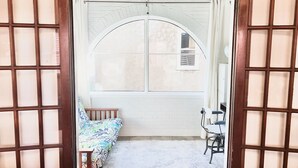 Une pièce dotée d’une grande fenêtre en arc de cercle, d’un lit avec une literie à motifs, d’une petite table et d’une chaise.