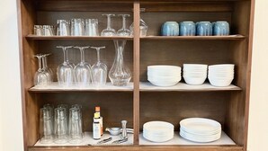 Un buffet en bois, de style bahut, doté d’étagères où sont disposés des verres à vin, une bouteille et un vase décoratif.