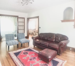 Un salon avec un canapé en cuir marron, deux fauteuils bleus, un tapis rouge à motifs et un plancher en bois.