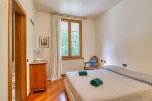 Ein Schlafzimmer mit einem Bett, einem Holzschrank, einem Stuhl, einem Fenster und einem Ventilator.