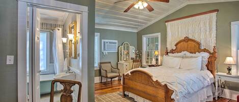 A bedroom with a wooden bed, a ceiling fan, a large mirror, and a view of the bathroom.