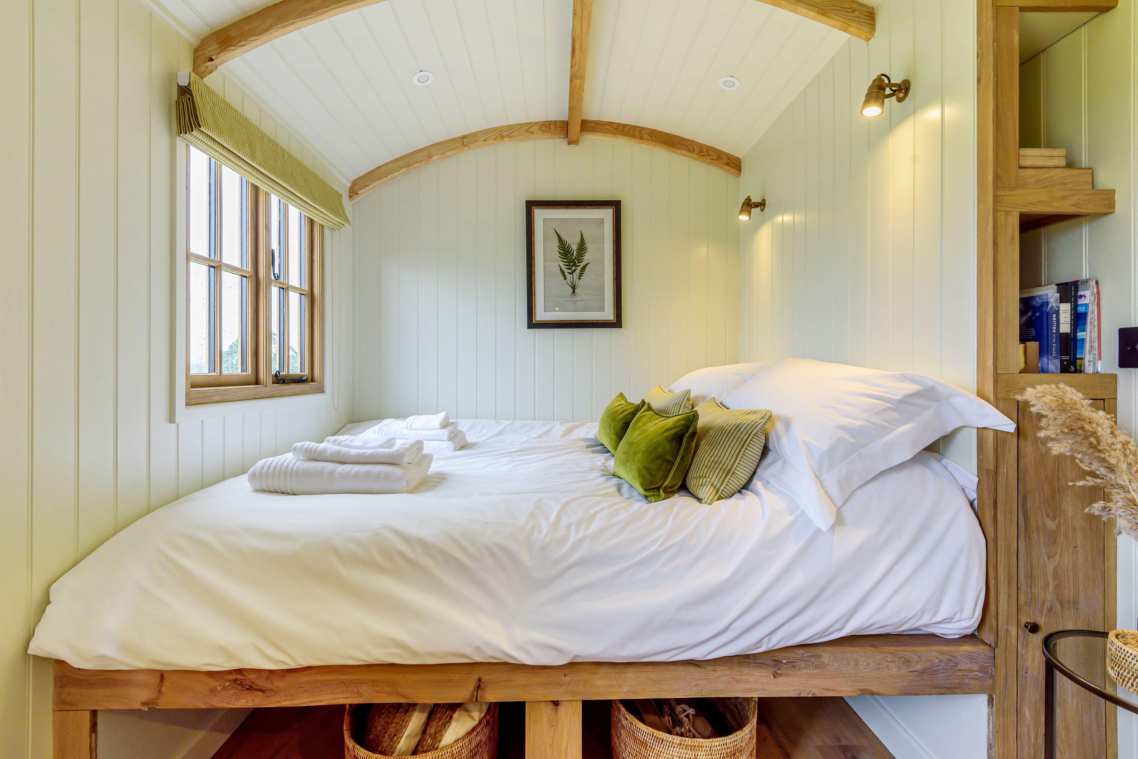 Une chambre avec un lit en bois, du linge de lit blanc et une plante décorative accrochée au mur.