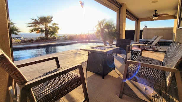 A poolside area with wicker furniture, a ceiling fan, and a view of the pool and palm trees. - "Hacienda Hangout"~ 5⭐RETREAT ~ PETS OK 🐾  VIEWS - POOL - SPA - BORDERS BLM  (Lake Havasu City)