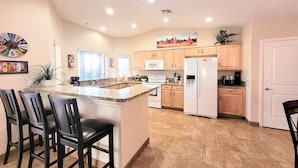 A kitchen with a central island, wooden cabinets, a refrigerator, and a clock on the wall. - "Hacienda Hangout"~ 5⭐RETREAT ~ PETS OK 🐾  VIEWS - POOL - SPA - BORDERS BLM  (Lake Havasu City)