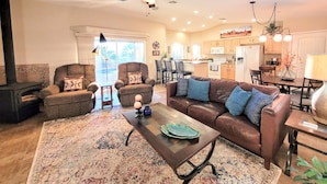 A spacious living room with a brown leather sofa, two armchairs, a coffee table, and a large window. - "Hacienda Hangout"~ 5⭐RETREAT ~ PETS OK 🐾  VIEWS - POOL - SPA - BORDERS BLM  (Lake Havasu City)