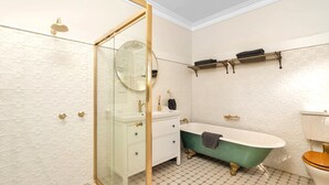 Un bagno con box doccia in vetro, una vasca da bagno indipendente, un mobile lavabo bianco con accessori dorati e un water con sedile in legno.