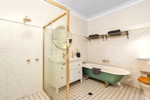 A bathroom with a glass shower enclosure, a freestanding bathtub, a white vanity with gold fixtures, and a toilet with a wooden seat. - Willow Tree Cottage. Bright, Airy & Jazzy. (Bundanoon)
