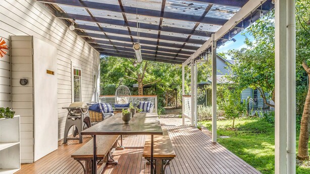 Un portico coperto con tavolo e panche in legno, un barbecue e una pergola con luci pendenti.