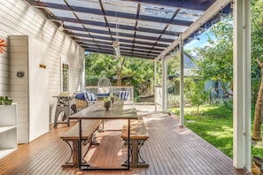Eine überdachte Terrasse mit einem Holztisch und Bänken, einem Grill und einer Pergola mit hängenden Lichtern.