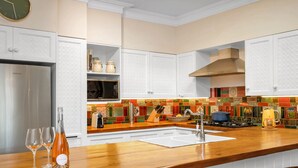 Una cucina con mobili bianchi, un frigorifero in acciaio inossidabile, un piano di lavoro in legno, un lavandino e un backsplash colorato.