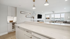 A modern kitchen with white cabinetry, a marble countertop, and pendant lighting. - Riverfront condo, Screen porch - Short walk across bridge to beach, shops, and restaurants! (Folly Beach)