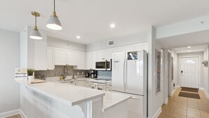 A modern kitchen with white cabinetry, a central island, and pendant lighting. - Riverfront condo, Screen porch - Short walk across bridge to beach, shops, and restaurants! (Folly Beach)
