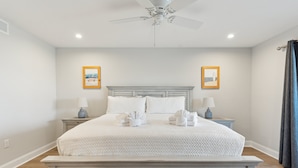 A bedroom with a large bed, two bedside tables with lamps, a ceiling fan, and two framed pictures on the walls. - Riverfront condo, Screen porch - Short walk across bridge to beach, shops, and restaurants! (Folly Beach)