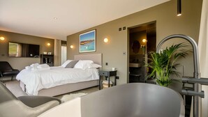 A modern hotel room with a large bed, a sitting area with a chair, a bathtub, and a view of the sea. - Little Hayloft by Bloom stays -  charming barn with hot tub (Canterbury)