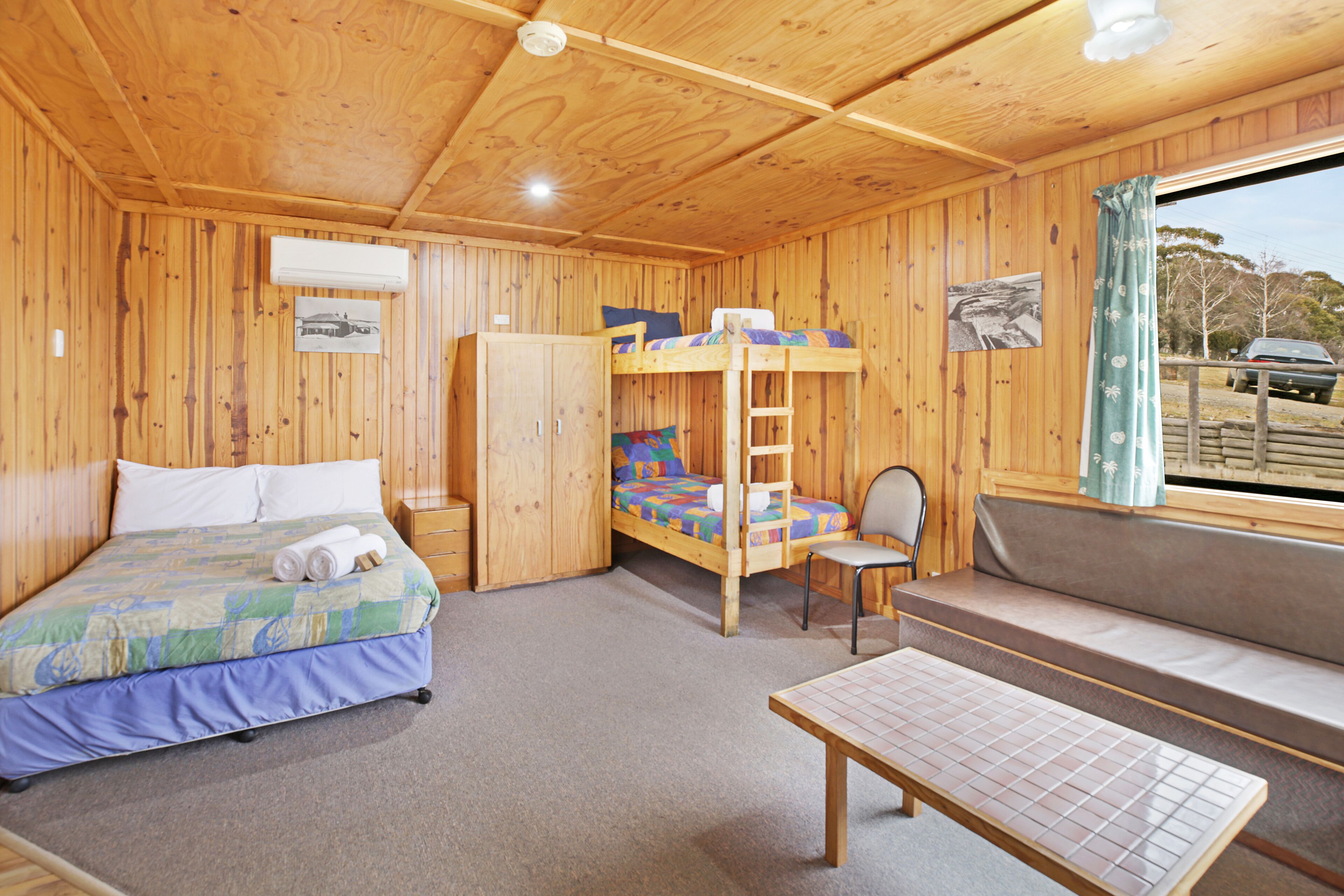 A wooden cabin room with bunk beds, a single bed, a table, and a window with a view.
