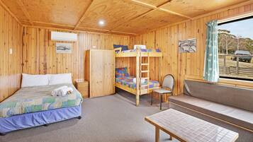 A wooden cabin room with bunk beds, a single bed, a table, and a window with a view.