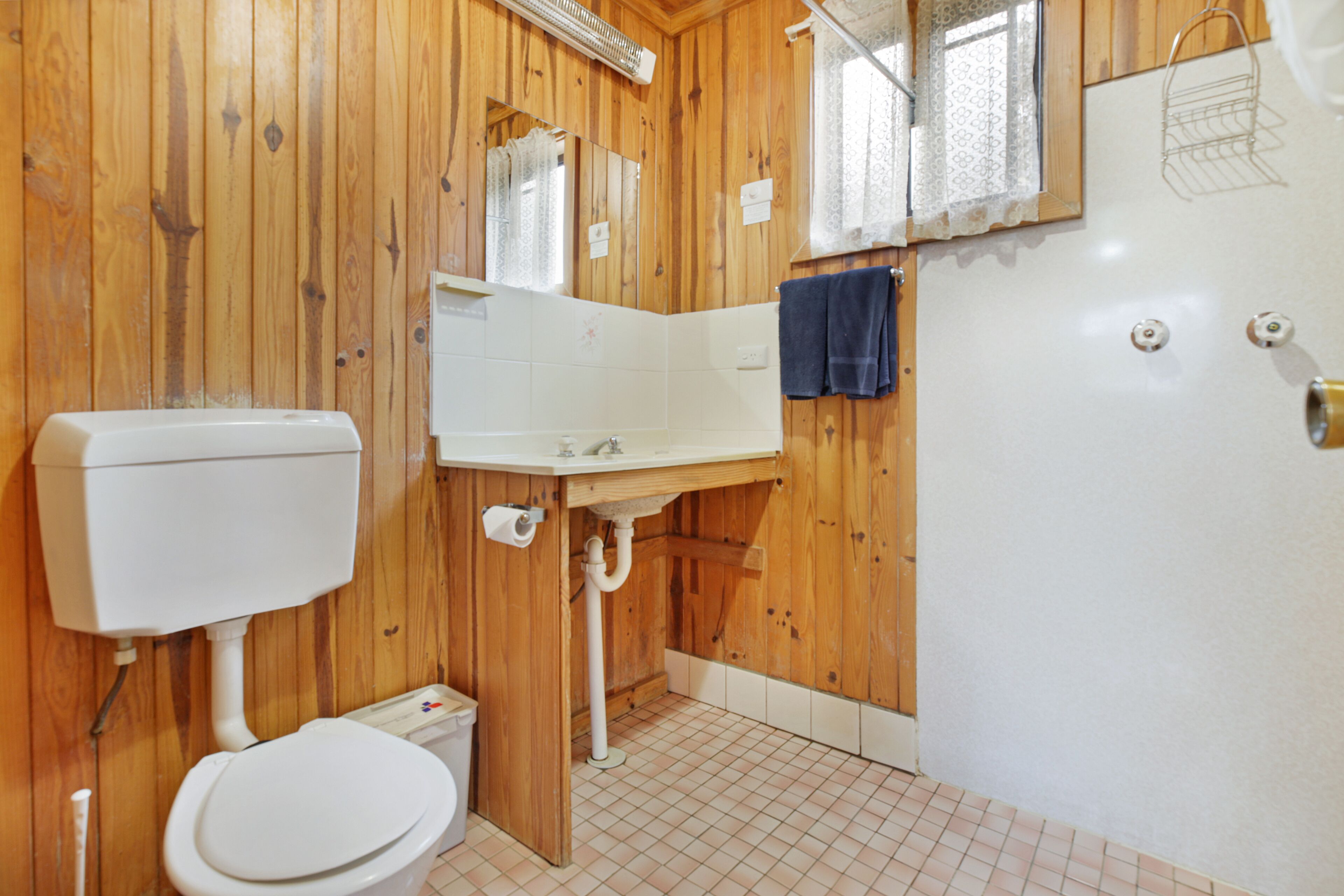 A wooden-paneled bathroom with a toilet, sink, and mirror.