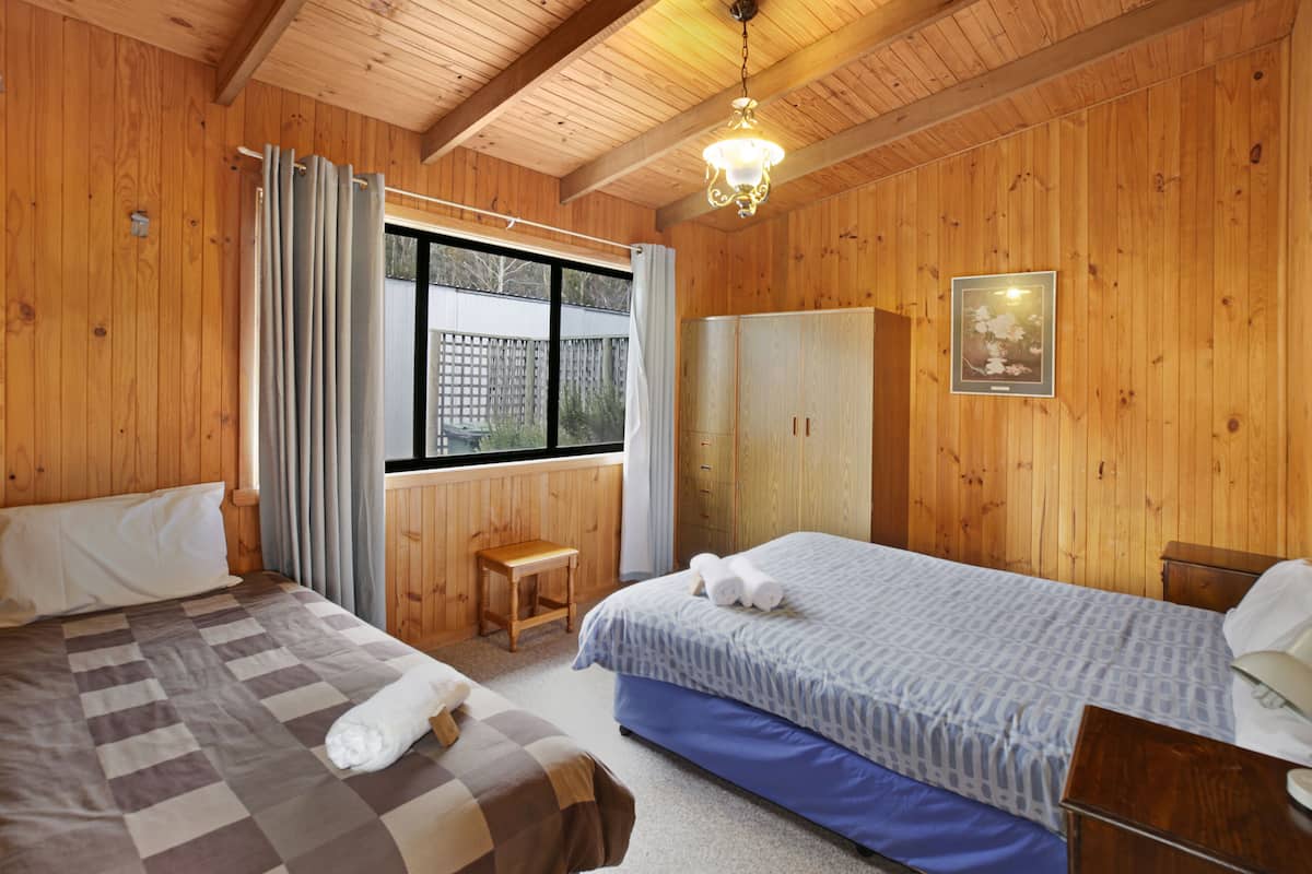A wooden room with two beds, a wooden bench, a wardrobe, and a window with curtains.