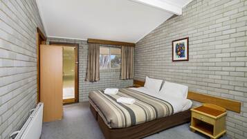 A bedroom with a bed, a wooden nightstand, a radiator, and a window with curtains.