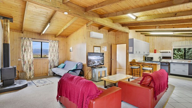 A cozy cabin interior with a wooden ceiling, a sofa set, a television, and a kitchen area. - Providence Park (Providence Portal)