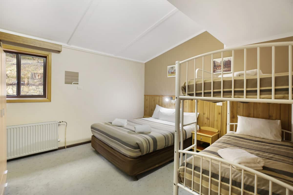 A room with bunk beds, a wooden headboard, a small bedside table, and a window with a view of trees.