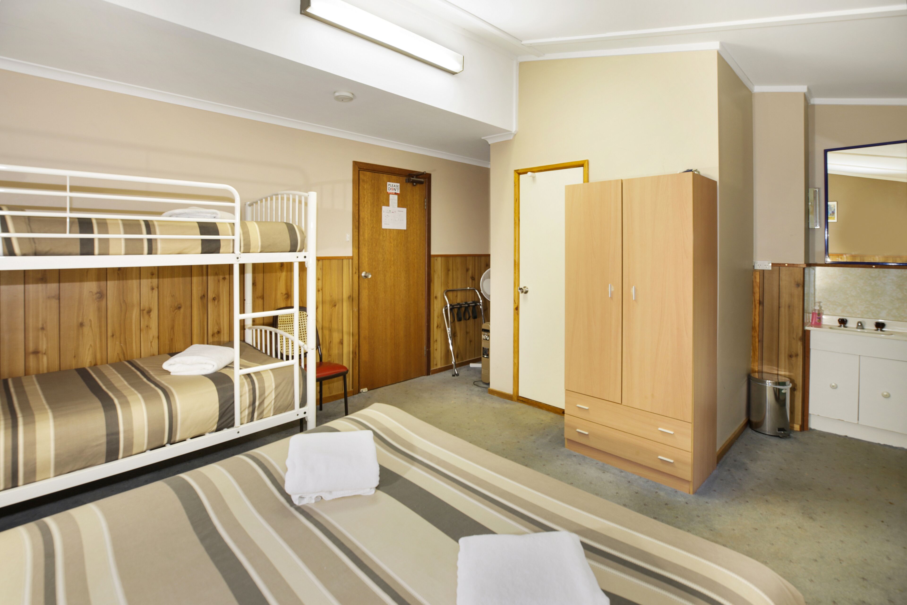 A room with bunk beds, a wooden wardrobe, a small desk, and a mirror.