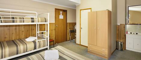 A room with bunk beds, a wooden wardrobe, a small desk, and a mirror.