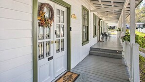 Een overdekte veranda met een witte gevel en groene details, een deur versierd met een krans, en een bordje met de tekst 'B&B'.