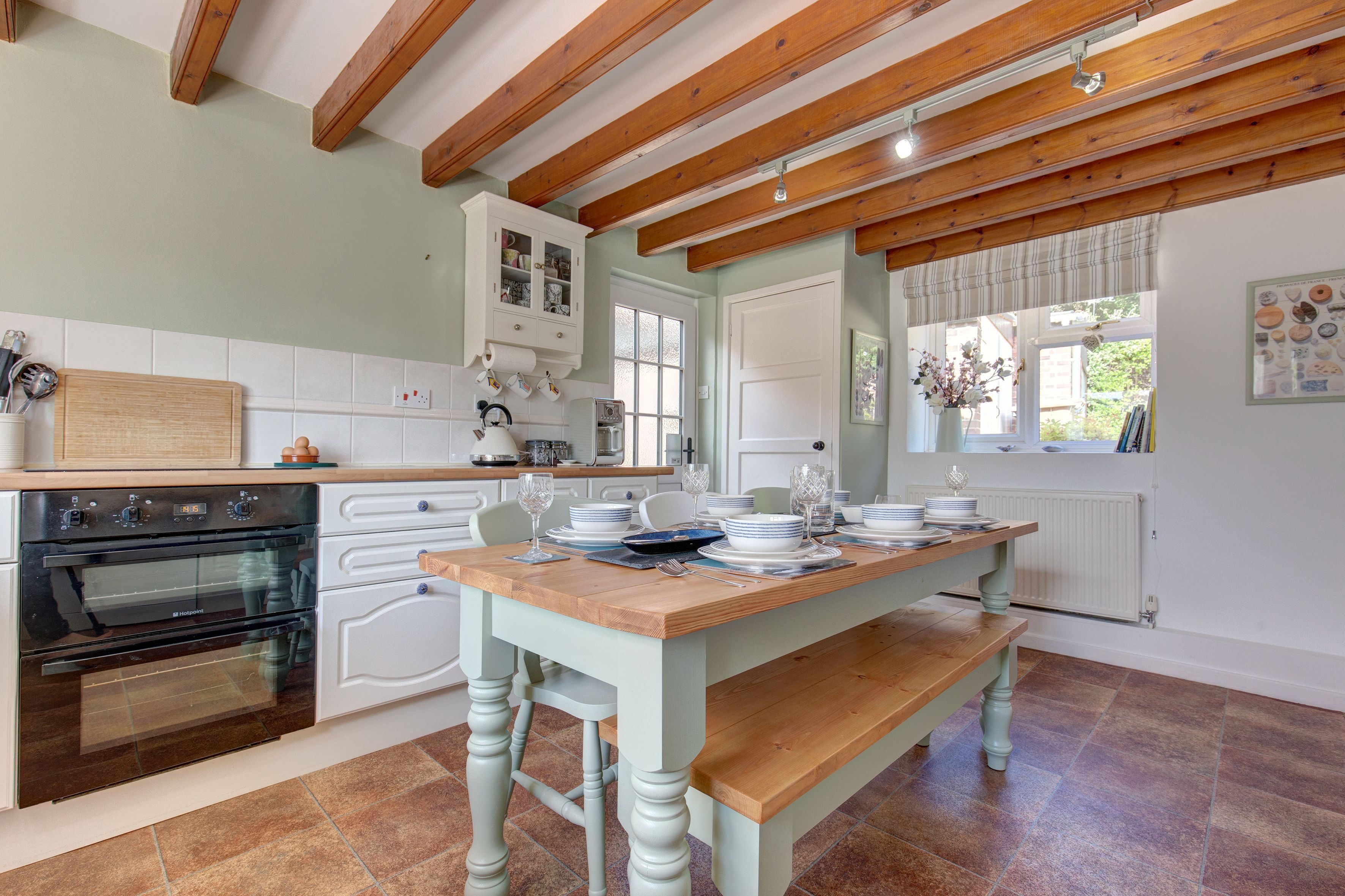 Une cuisine avec des poutres en bois, une table à manger dressée pour quatre personnes et un four encastré.