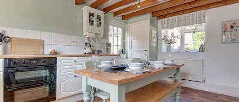 A kitchen with wooden beams, a dining table set for four, and a built-in oven.