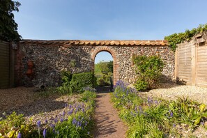A stone archway leading to a garden with a gravel path and purple flowers.
