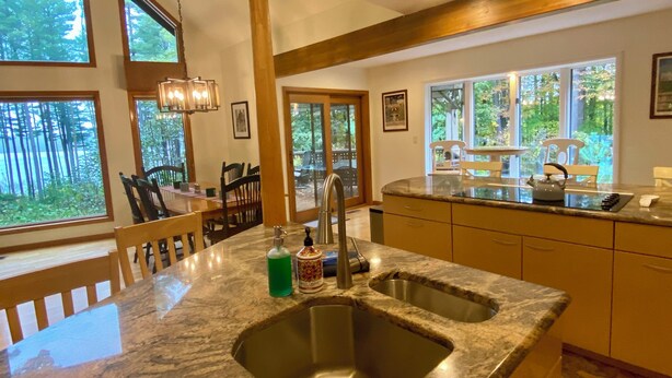 A kitchen with a granite countertop, stainless steel sink, and wooden cabinets. There are large windows providing natural light and views of the outdoors. - Lake View Berkshires Retreat - Private & Minutes to Lenox (Lee)