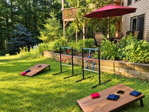 Un jardin avec une table en bois, deux fauteuils en forme de sac de haricots, un parasol rouge et une balançoire en métal.