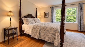 A four-poster bed with a floral bedspread, a bedside table with a lamp, and a window with curtains. - Lake View Berkshire Retreat – Private Setting Near Lenox (Lee)