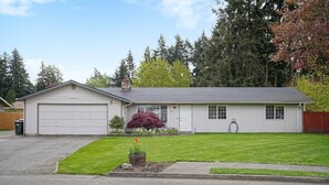 A single-story house with a garage, a front yard with a small garden, and a red-leaved bush. - Beautiful Stylish Home With Hot Tub (Puyallup)