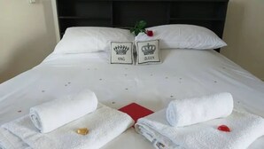 A neatly made bed with two pillows labeled "KING" and "QUEEN," a red book, and two towels with rose petals. - Panoramic Holidays - Deluxe 3 - Apartment with Outdoor Jacuzzi - Sea View (Peyia)
