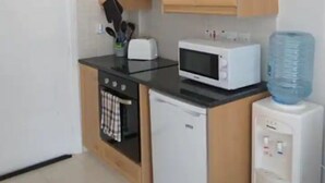 A compact kitchen with wooden cabinets, a microwave, a toaster, and a refrigerator. - Panoramic Holidays - Deluxe 3 - Apartment with Outdoor Jacuzzi - Sea View (Peyia)