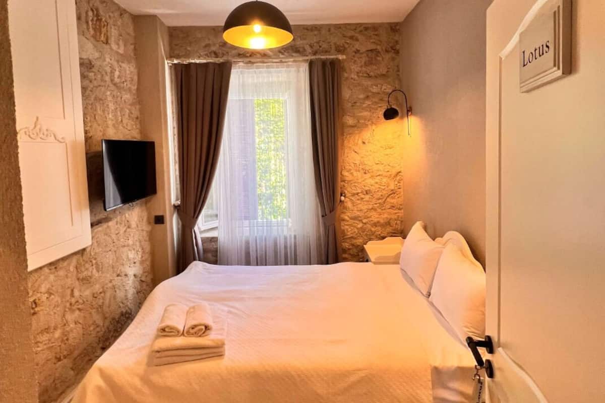 A bedroom with a bed, a TV, a stone wall, a window with curtains, and a sign on the door.