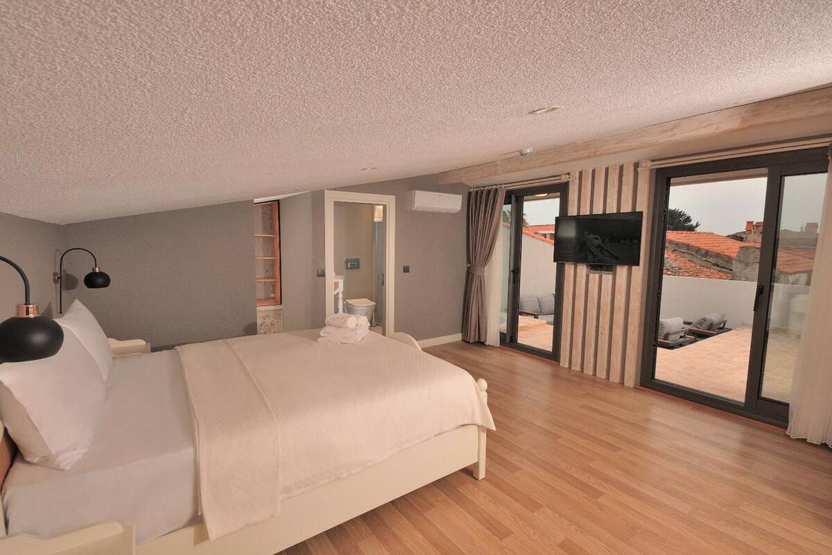 A modern bedroom with a large bed, a TV mounted on the wall, and a sliding glass door leading to an outdoor area.