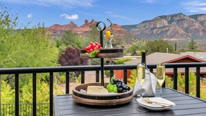 Un tavolo da pranzo con un vassoio di frutta, bicchieri da vino e una bottiglia su un balcone con vista sulle montagne.