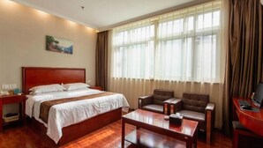 Een hotelkamer met een houten bed, een bureau met een computer, een stoel en een groot raam met gordijnen.