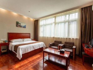 Une chambre d’hôtel avec un lit en bois, un bureau avec un ordinateur, une chaise et une grande fenêtre avec des rideaux.