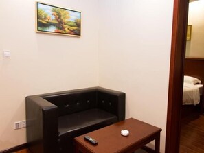Une pièce avec un canapé noir, une petite table en bois, une télécommande et un tableau accroché au mur.