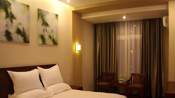Une chambre d’hôtel avec un grand lit, deux chaises, une table de chevet et une lampe fixée au mur.