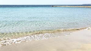 A beach with clear water, a sandy shore, and a distant breakwater.