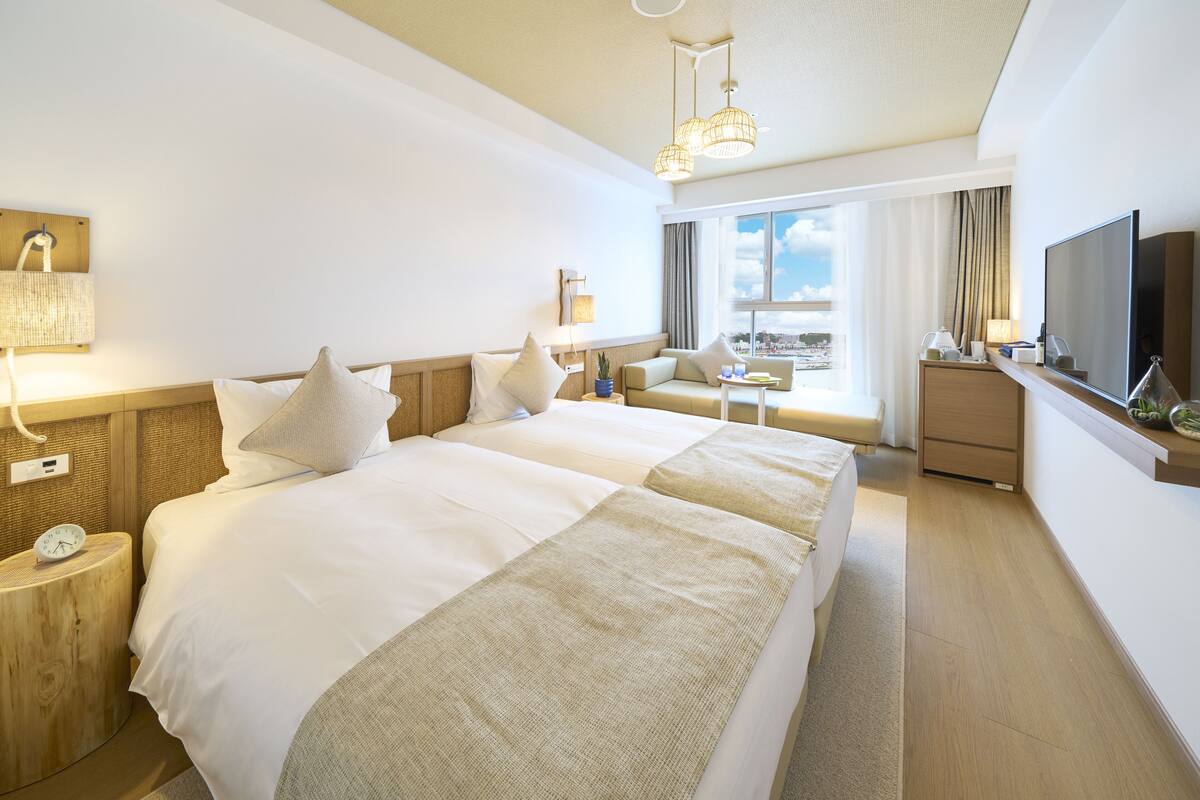 A hotel room with a large bed, bedside tables, a TV, and a view of the city.