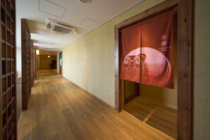 Un pasillo con piso de madera, una puerta de madera con cortina roja y un letrero que dice 'Women's Bath'.