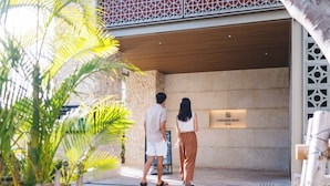 Um homem e uma mulher em frente à entrada de um hotel, com uma placa que diz 'HOTEL REOL TRINITY NAHA'.