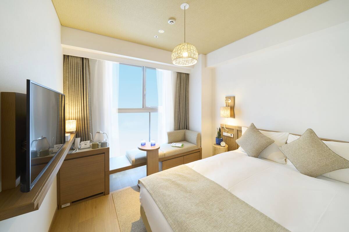 A hotel room with a bed, a desk, a television, a small table, and a window with curtains.