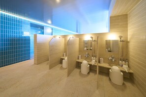 Un baño moderno con tres cabinas, un banco y un espejo sobre los lavamanos.